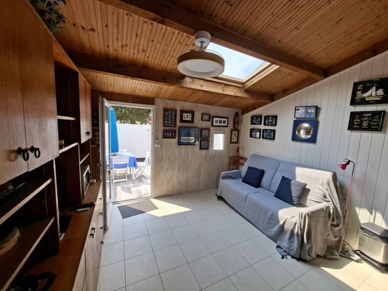 Séjour du studio aux Fermes Marines à Brétignolles-sur-Mer : canapé, plafond en bois et porte ouverte sur le patio